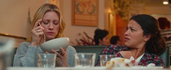 Movie still from “Someone Great” (2019), directed by Jennifer Kaytin Robinson – A woman sitting at a table with a plate in front of her face; Medium shot, Over the shoulder angle