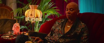 Movie still from “Someone Great” (2019), directed by Jennifer Kaytin Robinson – An older woman sitting on a red chair in front of a lamp; Medium shot, High angle