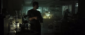 Movie still from “Spectral” (2016), directed by Nic Mathieu – A man standing in a dark room holding a knife; Medium shot, Low angle