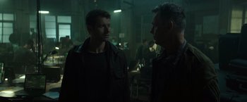 Movie still from “Spectral” (2016), directed by Nic Mathieu – Two men are standing in a room talking; Medium shot, Over the shoulder angle