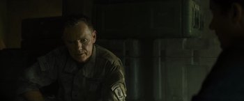 Movie still from “Spectral” (2016), directed by Nic Mathieu – A man in a military uniform sitting in front of a wall; Close Up shot, Over the shoulder angle