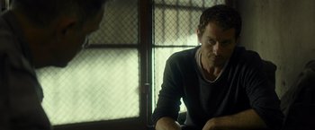 Movie still from “Spectral” (2016), directed by Nic Mathieu – A person sitting at a table in a room; Close Up shot, Over the shoulder angle