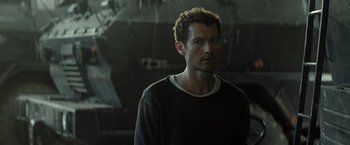 Movie still from “Spectral” (2016), directed by Nic Mathieu – A man standing in front of an airplane in the dark; Close Up shot, Over the shoulder angle