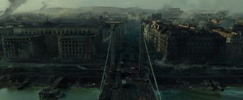 Movie still from “Spectral” (2016), directed by Nic Mathieu – An aerial view of an urban area with buildings and a river; Extreme Wide shot, High angle