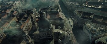 Movie still from “Spectral” (2016), directed by Nic Mathieu – An aerial view of a city with a large building; Extreme Wide shot, High angle