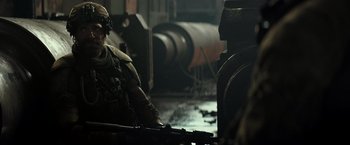 Movie still from “Spectral” (2016), directed by Nic Mathieu – A man sitting in front of a machine in a factory; Medium shot, Over the shoulder angle