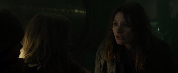 Movie still from “Spectral” (2016), directed by Nic Mathieu – A woman is sitting next to another woman in a dark room; Close Up shot, Over the shoulder angle