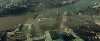 Movie still from “Spectral” (2016), directed by Nic Mathieu – A helicopter flying over a city with smoke billowing out of it; Extreme Wide shot, High angle
