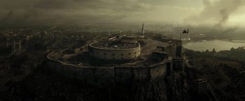 Movie still from “Spectral” (2016), directed by Nic Mathieu – An aerial view of an old castle with a statue in the background; Extreme Wide shot, High angle