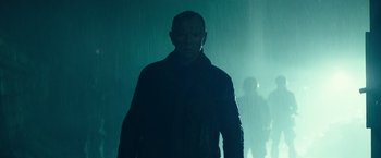 Movie still from “Spectral” (2016), directed by Nic Mathieu – A man standing in the rain in front of a green wall; Medium shot, Low angle