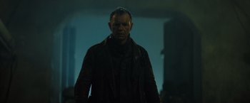 Movie still from “Spectral” (2016), directed by Nic Mathieu – A man wearing a leather jacket standing in a dark room; Medium shot, Low angle