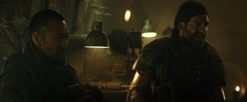 Movie still from “Spectral” (2016), directed by Nic Mathieu – A man in a leather jacket is sitting in front of some lights; Medium shot, Low angle
