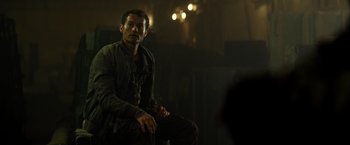 Movie still from “Spectral” (2016), directed by Nic Mathieu – A man sitting on a chair in a dark room; Medium shot, Over the shoulder angle