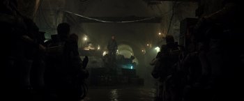 Movie still from “Spectral” (2016), directed by Nic Mathieu – A group of people standing around in a dark room; Wide shot, Low angle