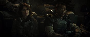 Movie still from “Spectral” (2016), directed by Nic Mathieu – A man and a woman sitting next to each other in the dark; Medium shot, Over the shoulder angle