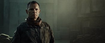 Movie still from “Spectral” (2016), directed by Nic Mathieu – A man in a military uniform standing in front of a brick wall; Close Up shot, Over the shoulder angle