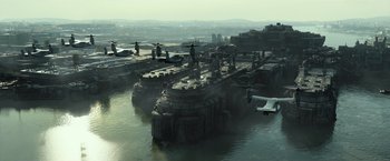 Movie still from “Spectral” (2016), directed by Nic Mathieu – An aerial view of an abandoned harbor with a plane flying by; Extreme Wide shot, High angle