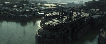 Movie still from “Spectral” (2016), directed by Nic Mathieu – An aerial view of a large building in the middle of a river; Extreme Wide shot, High angle