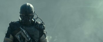 Movie still from “Spectral” (2016), directed by Nic Mathieu – A man with a helmet and goggles is standing; Close Up shot, Low angle