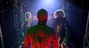 Movie still from “Spider-Man” (2002), directed by Sam Raimi – A man in a red jacket is standing in front of a group of women; Medium shot, Low angle