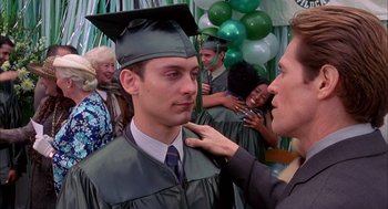 Movie still from “Spider-Man” (2002), directed by Sam Raimi – A man in a graduation cap and gown is getting his hair combed by a woman; Close Up shot, Over the shoulder angle