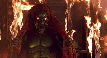 Movie still from “Spider-Man” (2002), directed by Sam Raimi – A man with a red head covering is standing in front of a fire; Medium shot, Low angle