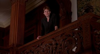 Movie still from “Spider-Man” (2002), directed by Sam Raimi – A man standing on top of a wooden railing next to stairs; Medium shot, Low angle