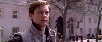 Movie still from “Spider-Man 2” (2004), directed by Sam Raimi – A man in a gray jacket is standing in front of a building; Close Up shot, Over the shoulder angle