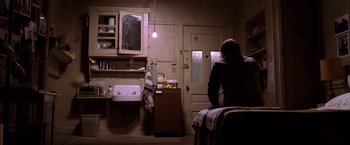 Movie still from “Spider-Man 2” (2004), directed by Sam Raimi – A man sitting on a bed in front of an open door; Wide shot, Low angle