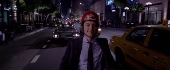 Movie still from “Spider-Man 2” (2004), directed by Sam Raimi – A man in a suit and a helmet is riding a scooter down the street; Medium shot, High angle