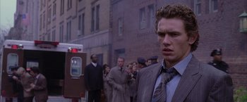 Movie still from “Spider-Man 2” (2004), directed by Sam Raimi – A man in a suit and tie standing in front of a group of people; Close Up shot, Over the shoulder angle
