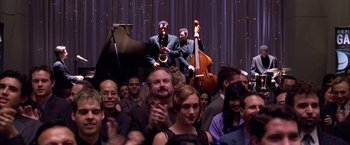 Movie still from “Spider-Man 2” (2004), directed by Sam Raimi – A group of people standing in front of a stage with musical instruments; Wide shot, Over the shoulder angle