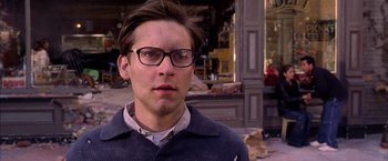 Movie still from “Spider-Man 2” (2004), directed by Sam Raimi – A man wearing glasses and a sweater standing in front of a building; Close Up shot, High angle