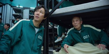 Movie still from “Squid Game” (2021), created by Hwang Dong-hyuk – A man and a woman sitting on top of a bunk bed; Medium shot, High angle