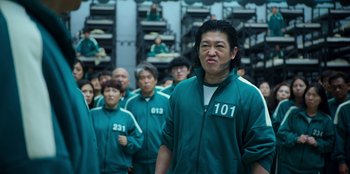 Movie still from “Squid Game” (2021), created by Hwang Dong-hyuk – A group of people in green jackets standing in a room; Medium shot, Low angle