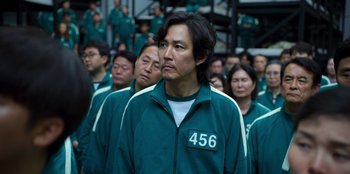 Movie still from “Squid Game” (2021), created by Hwang Dong-hyuk – A group of people in green jackets standing next to each other; Close Up shot, High angle