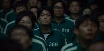 Movie still from “Squid Game” (2021), created by Hwang Dong-hyuk – A group of men in green jackets standing in a room; Close Up shot, High angle