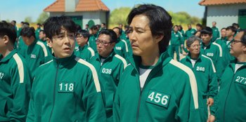 Movie still from “Squid Game” (2021), created by Hwang Dong-hyuk – A group of people in green jackets standing in front of a building; Close Up shot, Over the shoulder angle