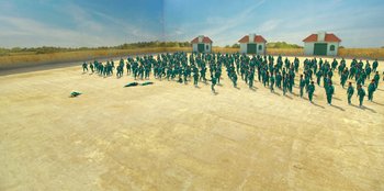 Movie still from “Squid Game” (2021), created by Hwang Dong-hyuk – A group of people standing on top of a dirt field; Extreme Wide shot, High angle