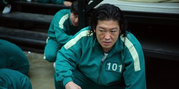 Movie still from “Squid Game” (2021), created by Hwang Dong-hyuk – A man in a green jacket sitting on the ground; Medium shot, High angle