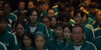 Movie still from “Squid Game” (2021), created by Hwang Dong-hyuk – A large group of people wearing green jackets; Wide shot, High angle