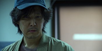 Movie still from “Squid Game” (2021), created by Hwang Dong-hyuk – A person wearing a hat; Close Up shot, Low angle