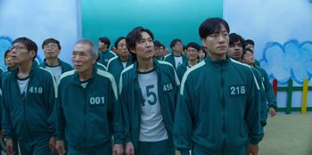 Movie still from “Squid Game” (2021), created by Hwang Dong-hyuk – A group of men standing next to each other in a room; Medium shot, High angle