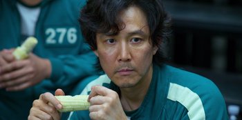 Movie still from “Squid Game” (2021), created by Hwang Dong-hyuk – A man holding a piece of corn in his hand; Close Up shot, Over the shoulder angle