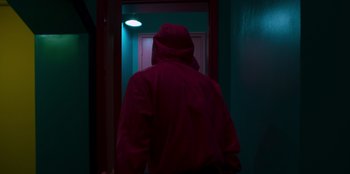 Movie still from “Squid Game” (2021), created by Hwang Dong-hyuk – A person wearing a hooded jacket walking through a doorway; Medium shot, Low angle