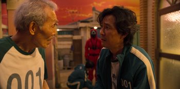 Movie still from “Squid Game” (2021), created by Hwang Dong-hyuk – Two men talking to each other in front of a red sky; Medium shot, Over the shoulder angle