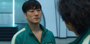 Movie still from “Squid Game” (2021), created by Hwang Dong-hyuk – A man in a green and white jacket looking at another man in a blue shirt; Close Up shot, Over the shoulder angle