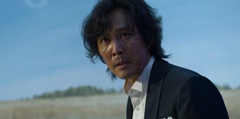 Movie still from “Squid Game” (2021), created by Hwang Dong-hyuk – A person wearing a suit and tie; Close Up shot, Over the shoulder angle