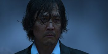 Movie still from “Squid Game” (2021), created by Hwang Dong-hyuk – A person wearing a suit and tie; Close Up shot, Low angle