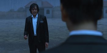 Movie still from “Squid Game” (2021), created by Hwang Dong-hyuk – A man wearing a suit and tie standing in front of a man in a suit; Medium shot, Over the shoulder angle